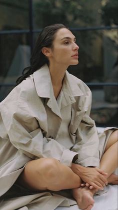 a woman sitting on top of a bed wearing a trench coat and matching heels with her legs crossed