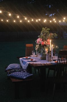 an outdoor dinner table set with candles and flowers on it, surrounded by string lights