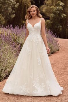 a woman in a white wedding dress standing on a dirt road with lavender bushes behind her