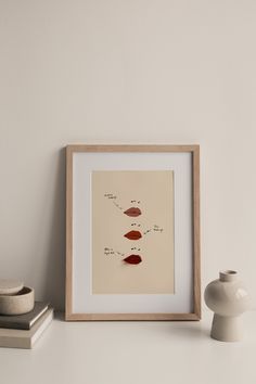 a white vase sitting on top of a table next to a framed print with different lipstick types