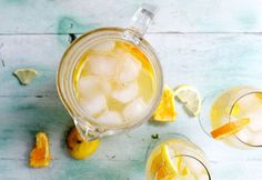 two glasses filled with lemonade and ice sitting on top of a wooden table next to sliced oranges