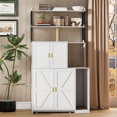 a white bookcase with doors and shelves next to a potted plant