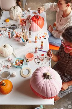 two women sitting at a table painting pumpkins