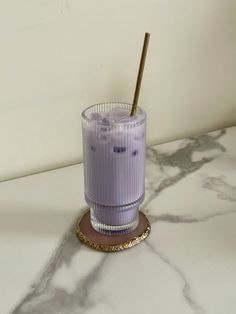 a purple drink sitting on top of a marble counter next to a gold rimmed cup