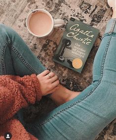 a woman sitting on the floor next to a book and cup of coffee with her legs crossed