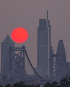 the sun is setting over a city with tall buildings in the background and a bridge stretching into the distance