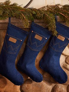 three pairs of blue jeans hanging from a mantel with pine branches and rocks in the background