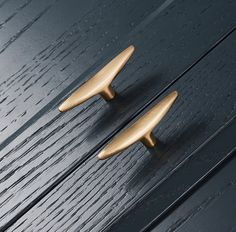 two brass door handles on a black painted wooden surface, one has a curved handle and the other has a pointed finial