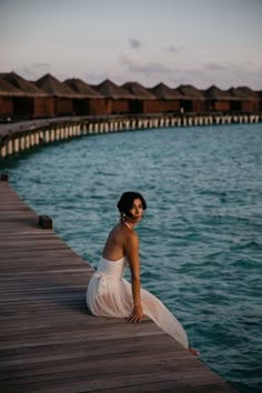 a woman is sitting on a dock by the water