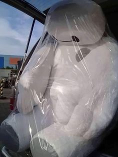 a large white teddy bear wrapped in plastic sitting in the back seat of a car