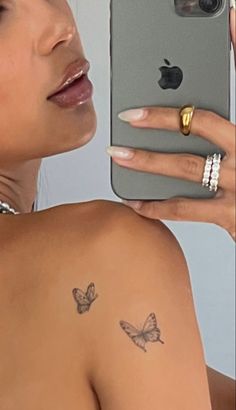 a woman holding up her cell phone to take a selfie with the butterfly tattoo on her arm