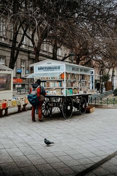 a person standing next to a cart with books on it in front of a tree