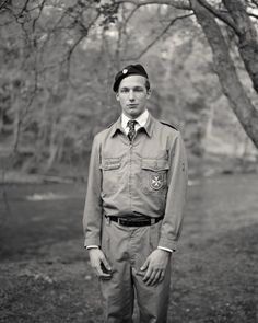 a black and white photo of a man in uniform standing under a tree with his hands on his hips