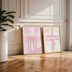 two pink posters are on the floor next to a white vase with a plant in it