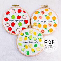 three embroidered fruit hoop art pieces with the words apples, oranges, and lemons on them