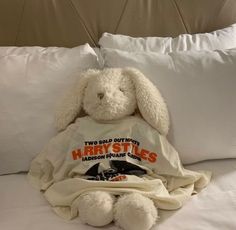 a white stuffed rabbit sitting on top of a bed under a blanket with harry potter t - shirt