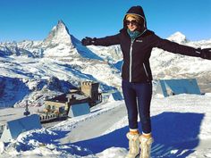 a woman standing on top of a snow covered slope with her arms outstretched in the air