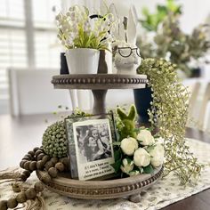 three tiered tray with flowers and photos on it in front of a dining room table