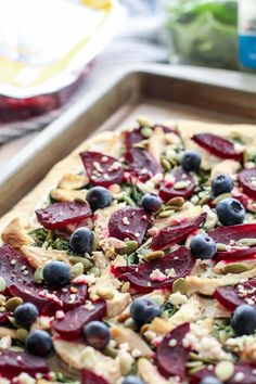 a pizza topped with beets, blueberries and pistachio