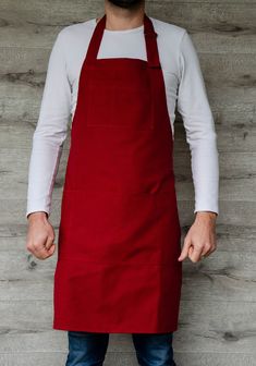 a man wearing an apron standing in front of a wooden wall with his hands on his hips