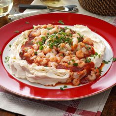 a red plate topped with shrimp covered in sauce and garnished with parsley