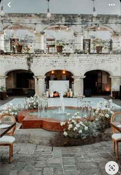 a fountain surrounded by chairs and tables in front of an old building with lots of windows