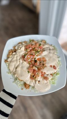 a person holding up a plate of food with dressing on top and vegetables in the middle