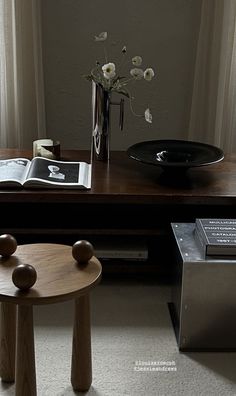 a wooden table topped with a vase filled with white flowers sitting next to a book