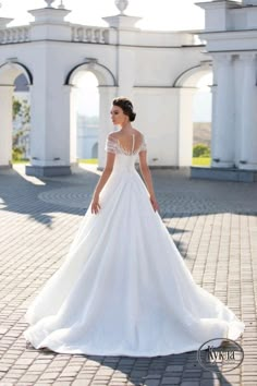 a woman in a white wedding dress is standing on a brick walkway and looking off into the distance