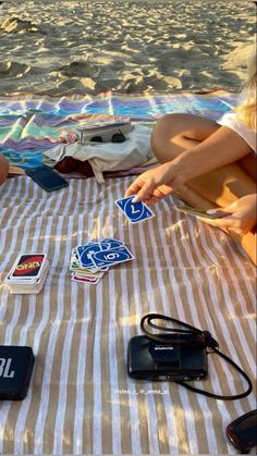 two people sitting on a beach towel playing with their cell phones and other electronic devices