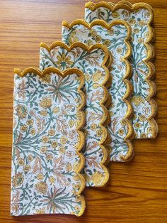 three placemats on a wooden table with floral designs in gold and green colors