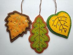 three felt leaf ornaments hanging from strings on a white surface with green and yellow accents