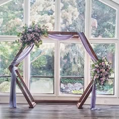 an arch decorated with flowers and ribbons in front of a large window at a wedding