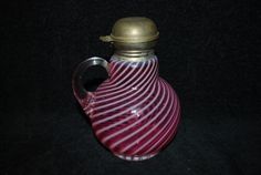 a red and white striped glass vase with a gold lid sitting on a black surface