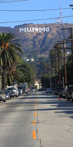 cars parked on the side of a road with hollywood sign in the background and palm trees lining the street