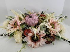 an arrangement of flowers and foliage on a white surface with a pumpkin in the center