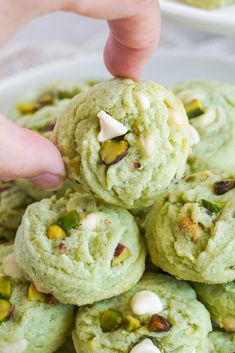 a person picking up some green cookies from a white plate with pistachios on top