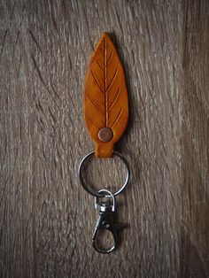 an orange leather leaf shaped keychain hanging from a metal hook on a wooden surface