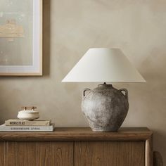 a table lamp sitting on top of a wooden dresser next to a book and vase