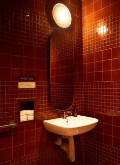 a sink and mirror in a bathroom with red tiles on the walls, along with toiletries