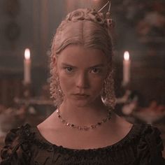 a woman with blonde hair wearing a tiara and looking at the camera while standing in front of candles