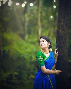 a woman in a blue and green sari standing next to a tree with the caption, what is she doing?