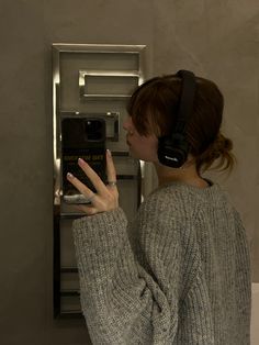 a woman wearing headphones is looking at her cell phone in front of an atm machine