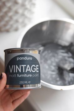 a hand holding a can of paint next to a metal bowl with something in it