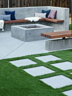 a concrete bench sitting next to a fire pit on top of a lush green field