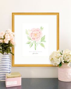 some flowers are sitting on a table in front of a framed print and vases