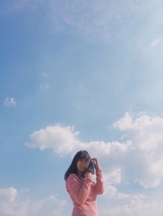 a woman standing on top of a sandy beach holding a camera up to her face