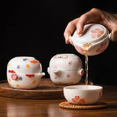 a person pouring tea from a teapot into a bowl on top of a wooden table