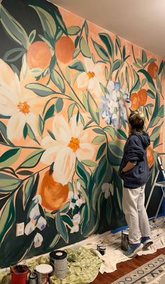 a man painting a mural on the side of a wall with flowers and oranges