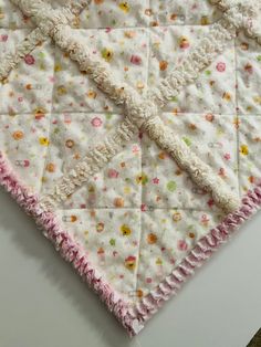 a close up of a quilt on a white table cloth with pink and yellow flowers